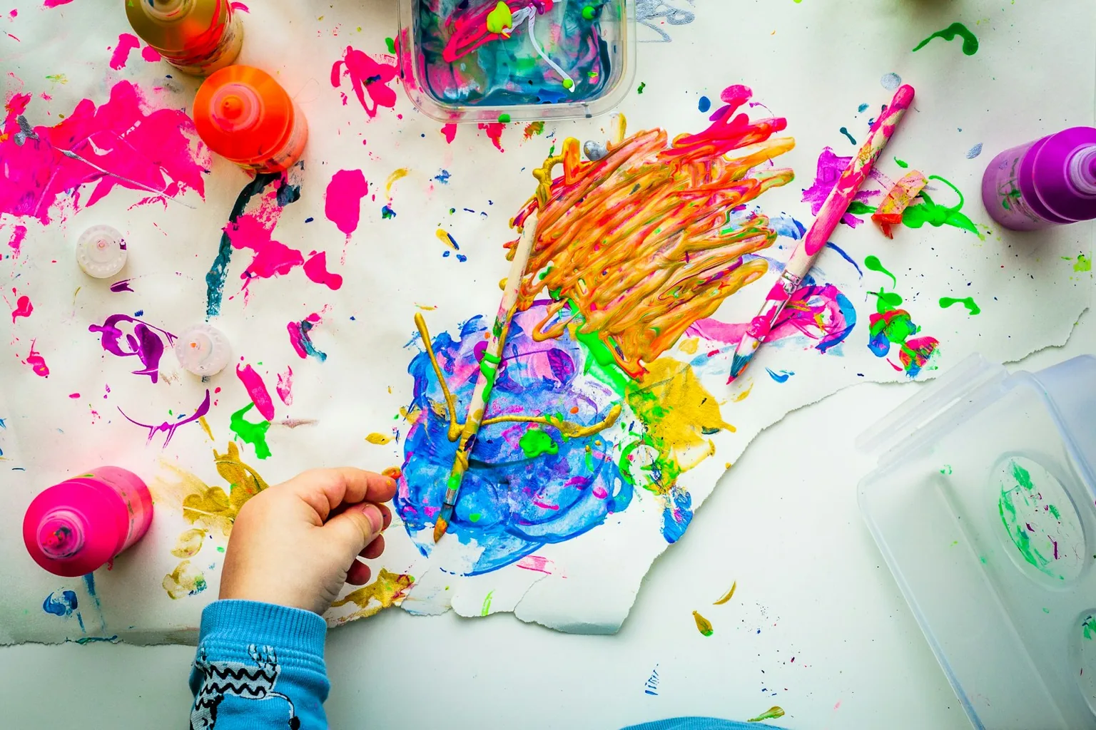 A child's paint-covered hand pressed onto a bright, splattered sheet of paper