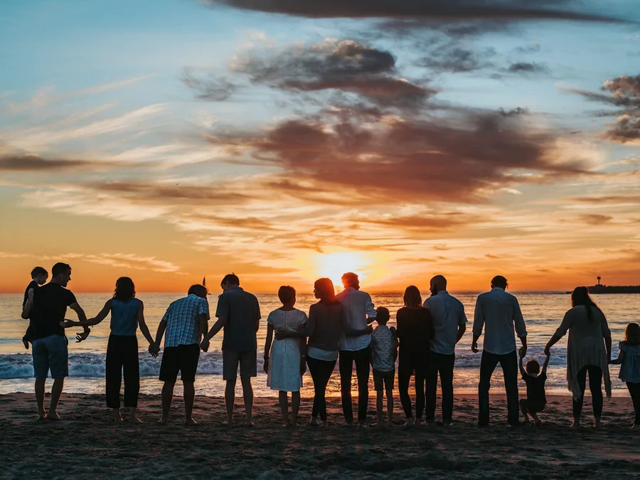 A long line of families holding hands on a beach at sunset
