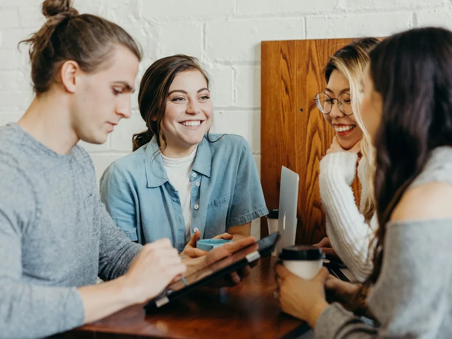 Three parents laughing together around a kitchen table with their phones out